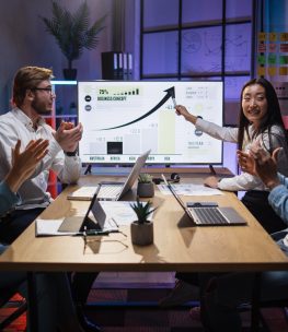 Asian woman showing financial report for colleagues Asian woman presenting financial report of worldwide economy on big monitor during meeting with international partners. Diverse colleagues sitting at desk and appealing to her speech.